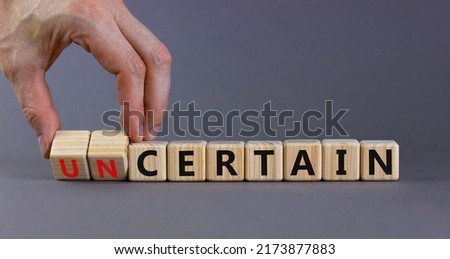 Certain or uncertain symbol. Businessman turns wooden cubes and changes the concept word uncertain to certain. Beautiful grey table, grey background, copy space. Business certain or uncertain concept.