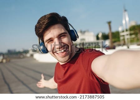 Close up young strong sporty fit sportsman man in t-shirt headphones do selfie shot mobile cell phone show landscape warm up train at sunrise sun dawn over sea beach outdoor on pier seaside in morning