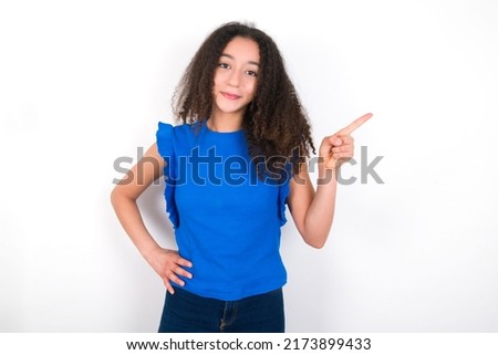 Teenager girl with afro hair style wearing blue t-shirt over white background looking at camera indicating finger empty space sales