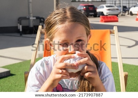 A child is drinking a cola and eating a burger in the recreation area. Rest on the summer playground. Picnic for children. Rest zone.