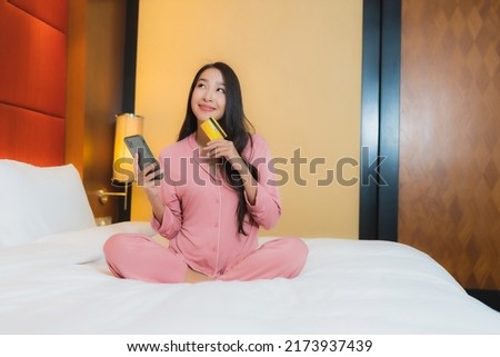 Portrait beautiful young asian woman use smart mobile phone with credit card on bed in bedroom interior