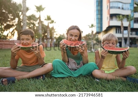 Sweet family, mother and her kids eating watermelon outdoor and having fun. High quality photo