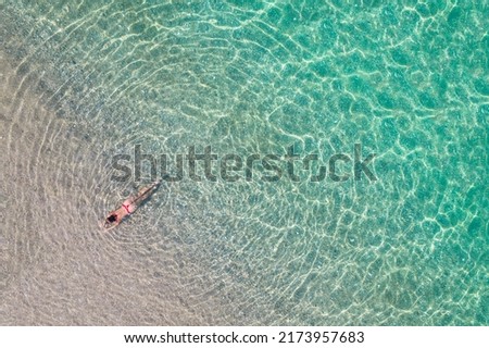 Top, aerial view. Young beautiful woman in a red bikini panties lying and sunbathe in sea water on the sand beach. Drone, copter photo. Summer vacation. View from above. 