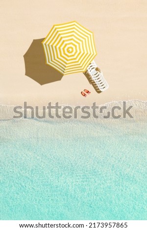 Aerial view of sunbed, lounge, yellow umbrella, flip flops on sandy beach. Summer and travel concept. Blue, turquoise transparent water surface of ocean, sea, lagoon. Aerial, drone view. vertical Royalty-Free Stock Photo #2173957865