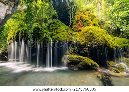 Lost waterfall inside the forest, enchanting place for real adventures. River flows quietly through the wilderness forest creating a waterfall among the yellow and red green mosses. Green moss