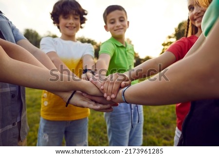 Bunch of children playing together on a good summer day. Group of happy friends standing in a circle in a green park or field, smiling and stacking their hands. Cropped closeup shot. Teamwork concept Royalty-Free Stock Photo #2173961285