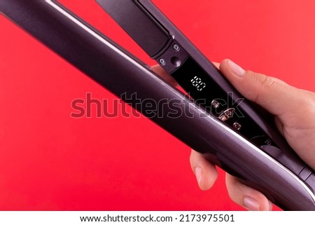 Millennial woman holding hair straightener with display 180 on red background, closeup. Panorama. Modern hair iron for straightening
