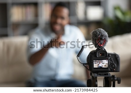 Close up African American blogger using digital camera, recording vlog, young man creating content for social network, business coach mentor speaking, shooting lecture, webinar sitting on couch Royalty-Free Stock Photo #2173984425