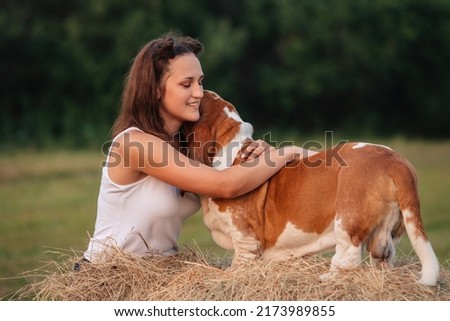 A young adult girl walks with a Basset Hound dog in nature. The owner hugs the pet. Royalty-Free Stock Photo #2173989855