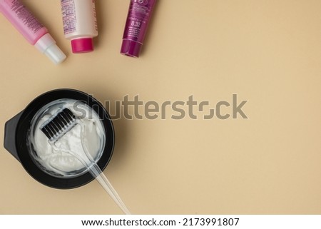 Flat lay of hairdresser equipment for mixing hair dye. Professional black jar with a brush on beige background. Preparing dye for hair coloring. Free space for text Royalty-Free Stock Photo #2173991807