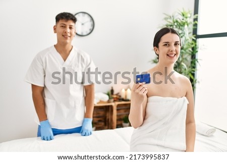 Woman smiling happy waiting to recive massage holding credit card at beauty center.