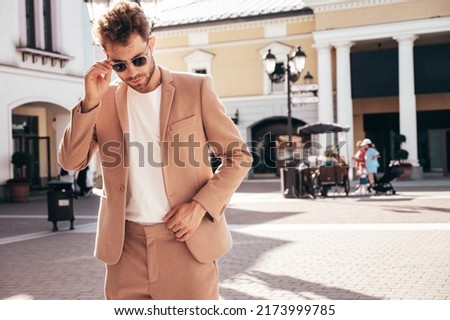 Handsome confident stylish hipster lambersexual model.Sexy modern man dressed in elegant beige suit. Fashion male posing in the street background in Europe city at sunset. In sunglasses Royalty-Free Stock Photo #2173999785