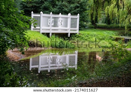 A white-painted fence reflecting on the surface of a pond in a park