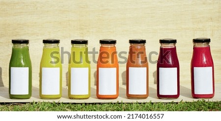 Cold-pressed juices, from many kinds of fresh fruits and vegetables that have been given different colors, are packed into glass bottles with blank white labels on wooden background. Royalty-Free Stock Photo #2174016557