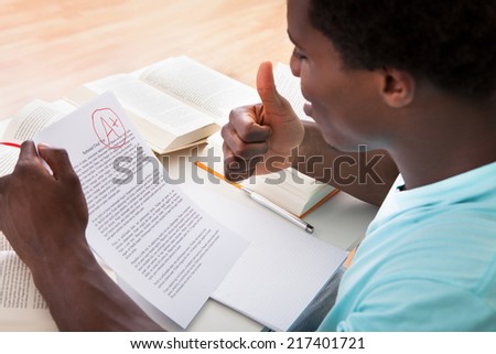Happy African Male Student Showing A Paper With Perfect Grade A Plus In Classroom Royalty-Free Stock Photo #217401721