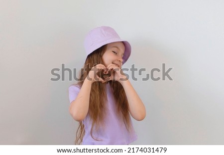 charming little girl in a summer hat makes a heartfelt gesture with her fingers with a happy sincere smile. Layout of the copy space. Showing the shape of the heart with your hands.