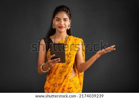 Young beautiful girl or woman holding and using smartphone or mobile or tablet phone on a grey background 