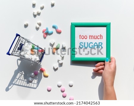 Frame with text Too Much Sugar in hand. Excess of sweets, chocolate, candy, sweet food. Various tasty snacks in pastel colors, pink, mint green, on white background. Text in pink square frame. Royalty-Free Stock Photo #2174042563