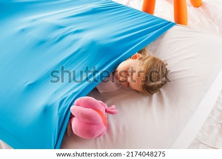 A cute blonde Caucasian girl sleeping on a mattress under a blue cozy blanket