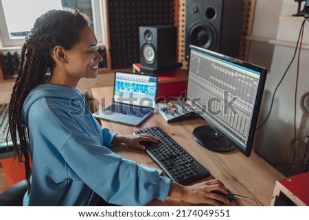 Beautiful young stylish female African audio engineer and producer working in music recording studio creating cool song Royalty-Free Stock Photo #2174049551