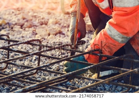 Builder's hands fixing steel reinforcement bars at construction site. Steel fixer assembling reinforcement cage. Selective focus Royalty-Free Stock Photo #2174058717