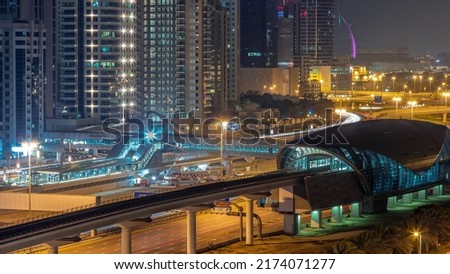 Futuristic building of Dubai metro station and luxury skyscrapers behind in Dubai Marina aerial night timelapse. Traffic on Sheikh Zayed road highway, United Arab Emirates