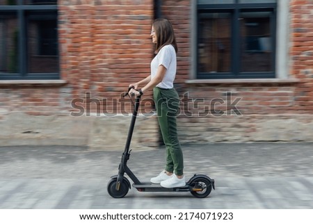 Woman in white t shirt and sneakers rides electric scooter Royalty-Free Stock Photo #2174071923