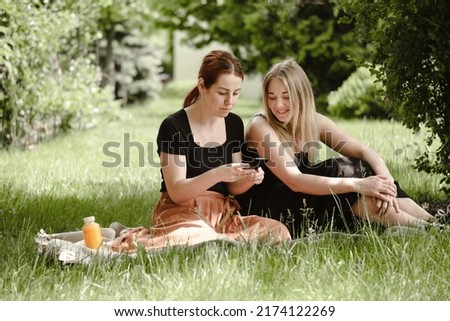 Two woman having fun on picnic. Friends on blanket communicating happily making selfie. Cheerfully female talk outdoors, People laughing and having rest in garden, park with smartphone