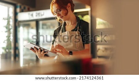 Cheerful shop owner using a digital tablet while standing in her grocery store. Successful female entrepreneur running her small business using wireless technology. Royalty-Free Stock Photo #2174124361