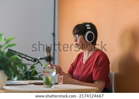 Mature woman making podcast recording for her online show. Attractive business woman using headphones front of microphone for a radio broadcast