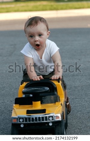 Adorable one year old boy pushes large toy car to help him walk while playing outside. This is a close up picture and he has a cute expression on his face.