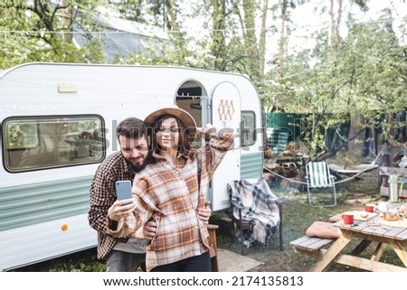 Young beautiful loving couple travelling across country in the van. Millennial man and woman in a travel camper. Cozy atmosphere, vacations vibe. Playing guitar, drinking tea, taking selfie photo