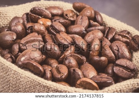 Heap of dark roasted coffee grains in jute bag on concrete structure. Vintage photo