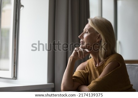 Pensive attractive middle-aged female resting on sofa at home looking out window having nostalgic mood, recollect, deep in thoughts, missing grown up children feeling loneliness. Retirement concept Royalty-Free Stock Photo #2174139375