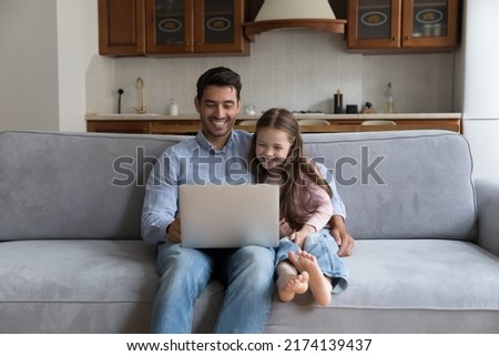 Hispanic father and preschool daughter sit on cozy sofa enjoy weekend with laptop, watch family movie, funny videovlog, laughing feels happy. Young generation use modern tech, leisure at home concept
