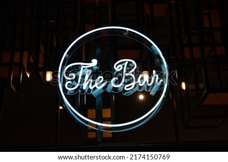 A white-colored neon sign saying 'the bar' on a dark background. A stylish abstract scene, for presentation background or advertisement purpose for nightlife topics. 