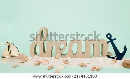 Bright sea sand decorated with shells, anchor, boat and dream letters on pastel green background. Minimal summer concept. Perfect summer party or peaceful ocean aesthetic layout. Dream vacation idea.