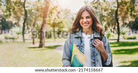 ukrainian student girl smiling and walking in the park. Cute yong woman holding folders and notebooks in hands. social training program. Learn english. web banner. copy space Royalty-Free Stock Photo #2174158667