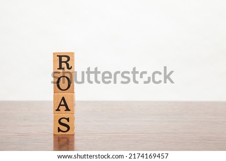 ROAS character. Return on investment. Return On Investment. Written on four wooden blocks. Black letters. Wooden table background.
