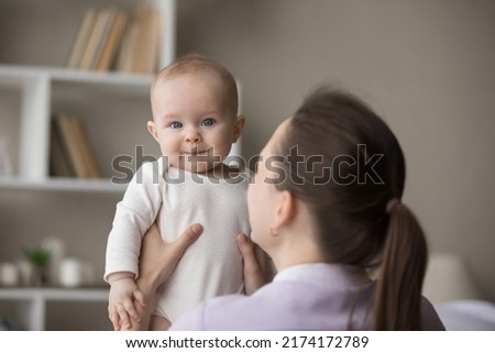 Rear back view young loving mom holding in arms her cute newborn, baby looks at camera. Family enjoy playtime together after daytime nap at home. Parent care, mothers love, infancy, motherhood concept Royalty-Free Stock Photo #2174172789