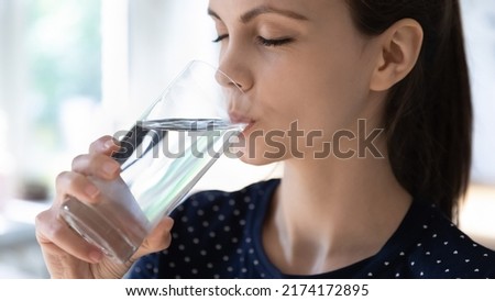 Peaceful thirsty pretty girl drinking fresh pure water at home, swallowing beverage with closed eyes, holding transparent glass, recovering hydration balance, keeping diet. Banner shot, close up Royalty-Free Stock Photo #2174172895
