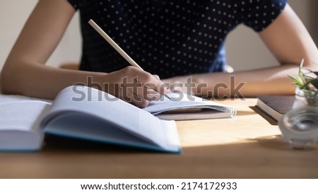 Young student girl preparing for college test, exam, writing notes, making draft, summary of textbook, studying, reading book for class report. Learning workplace table close up, banner shot Royalty-Free Stock Photo #2174172933