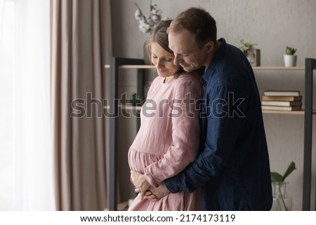 Loving future parents expecting their first baby hugging standing at home, caring husband touch belly of pregnant wife feel love, express caress to unborn child. Cherish, parenthood, new life concept Royalty-Free Stock Photo #2174173119