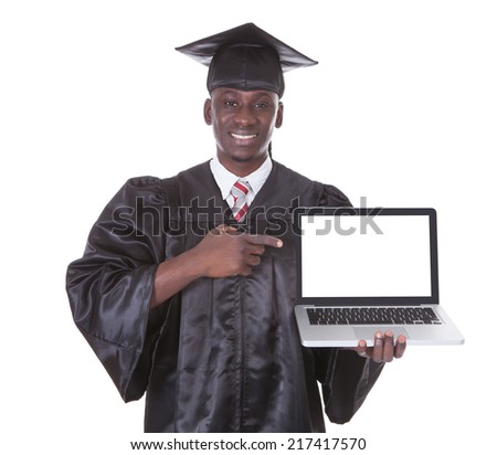 Male Student In Graduate Robe Pointing Towards Laptop Over White Background