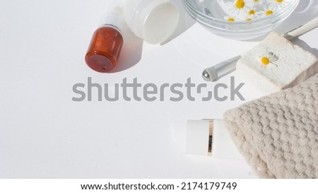 Beauty concept. Cream, serum for the face, cosmetic accessories for facial skin care and a glass transparent bowl with chamomile flowers on a white pastel background.Flat lay, top view, copy space