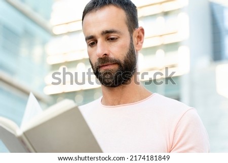Closeup portrait of pensive handsome student studying, learning language in university campus, education concept. Handsome bearded middle aged man reading book, planning project on the street 