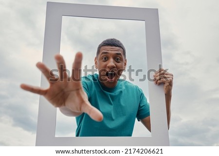 Playful mixed race man looking through a picture frame while standing outdoors