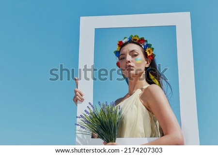 Attractive Ukrainian woman in floral crown holding picture frame with blue sky in the background