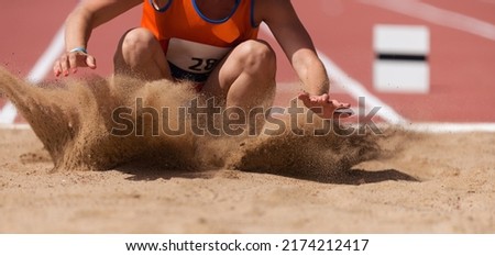 Female athlete long jump landing sand spray, landing in long jump in track and field Royalty-Free Stock Photo #2174212417