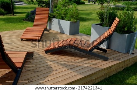 rocking chair on the pavement under the trees in the square. wooden deck chairs made of tropical wood for one person in the park. They are comfortable made of brown planks, slats steel frames, pine Royalty-Free Stock Photo #2174221341